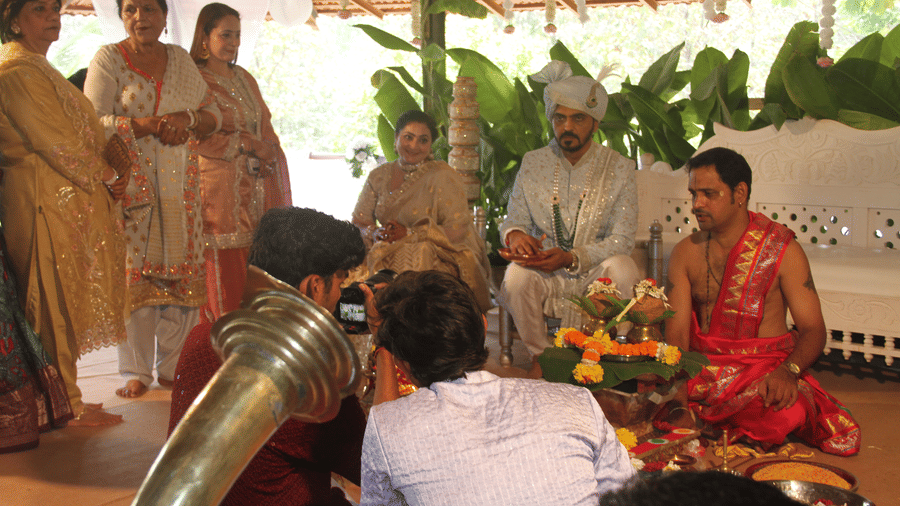 Groom in a cream sherwani seated beside a priest performing wedding rituals with marigold garlands and kalash pots at Golden Tulip Goa, Mandrem Beach.