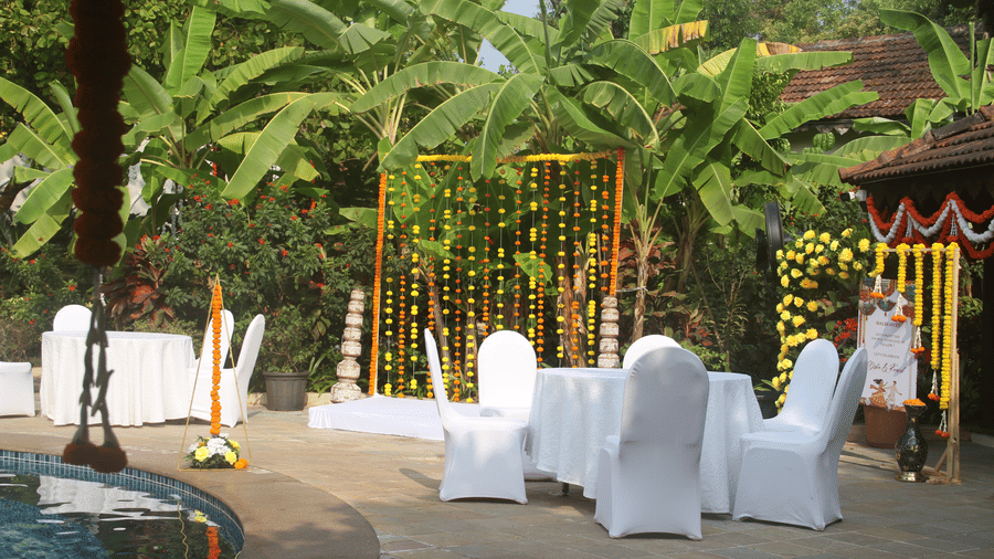 Haldi ceremony setup by the pool with white-draped chairs, a marigold-string backdrop, and banana trees at Golden Tulip Goa, Mandrem Beach.