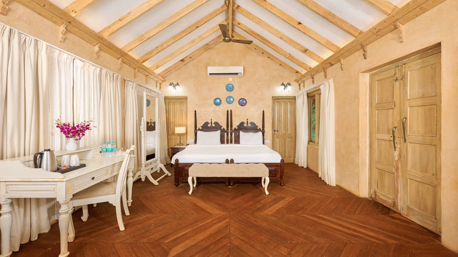 One Bedroom Pool Villa at Golden Tulip Goa, Mandrem Beach featuring a double size bed, a work and chair, tea and coffee maker with cup, and a mirror.