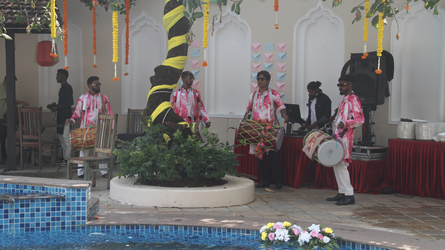 4 dhol drummers in pink floral outfits performing beside the pool with a DJ console and hanging marigold garlands at Golden Tulip Goa, Mandrem Beach.