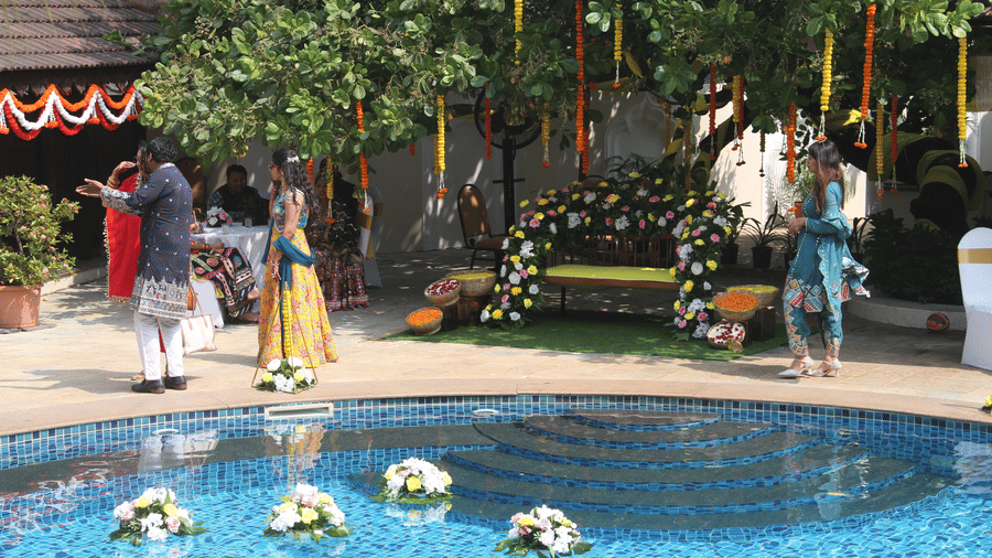 Guests in festive Indian wear beside the pool with floating flower bouquets and a flower-decked bench at Golden Tulip Goa, Mandrem Beach.