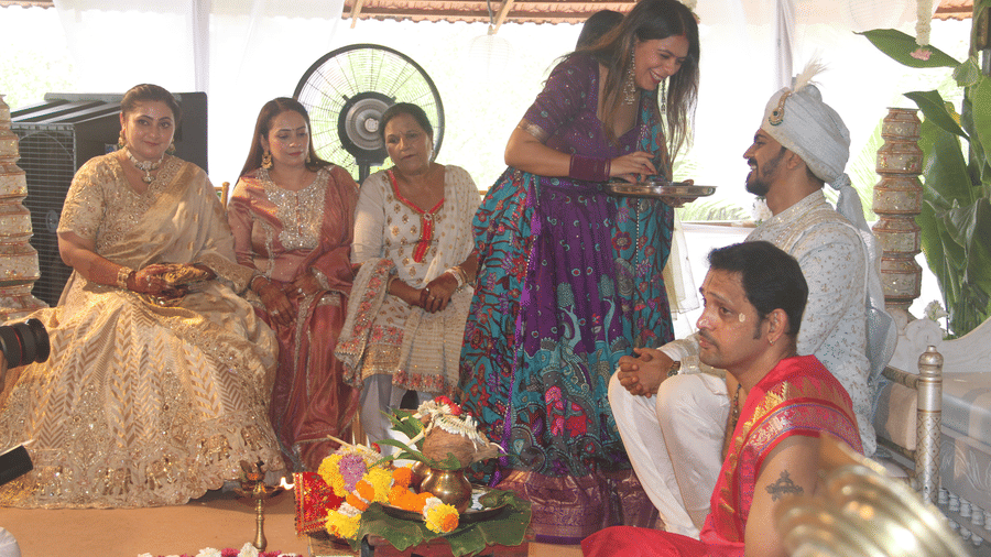 Woman holding a ritual plate toward the groom in a white sherwani during a wedding ceremony with flower garlands at Golden Tulip Goa, Mandrem Beach.