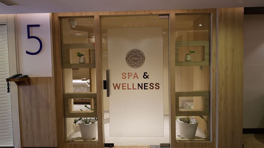 Glass door entrance to a spa and wellness centre labelled 'Aureum Spa & Wellness,' surrounded by wooden panelling, potted plants on display shelves, and a visible massage room in the background - Golden Tulip, Lucknow