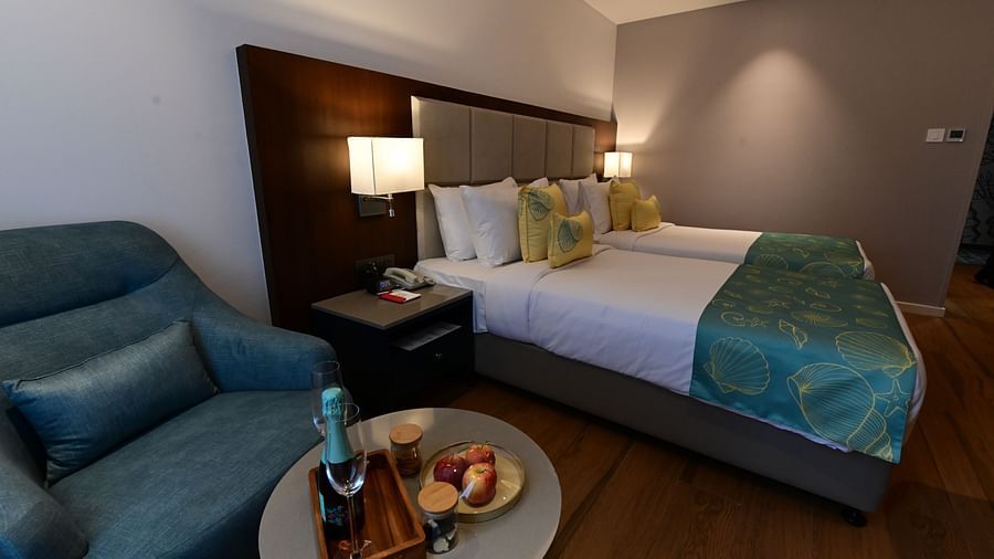 A room at Golden Tulip Vagator, Goa with twin beds, a sofa chair and a coffee table set up