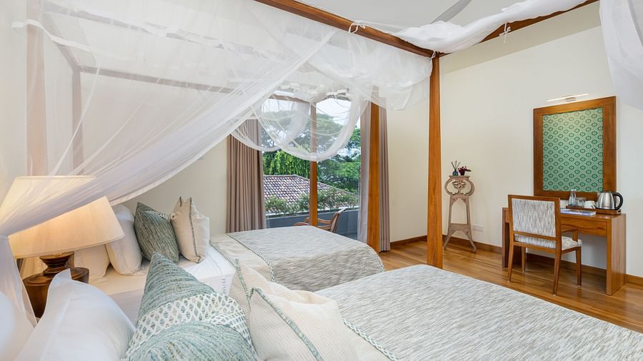 A serene bedroom featuring twin canopy beds, soft white linens, and large windows offering natural light - Deluxe Room at  Heavensa Villas and Suites by the Clarks, Galle