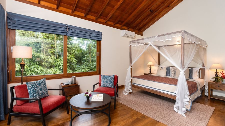 A spacious bedroom with high wooden ceilings, elegant furnishings, and a canopy bed, complemented by a large window with garden views - Family Suite Garden View at Heavensa Villas and Suites by the Clarks, Galle