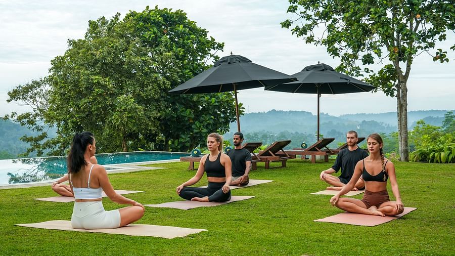 A group of people practising yoga outdoors on a lush lawn, with views of the surrounding hills and trees, providing a calming retreat - Heavensa Villas and Suites by the Clarks, Galle