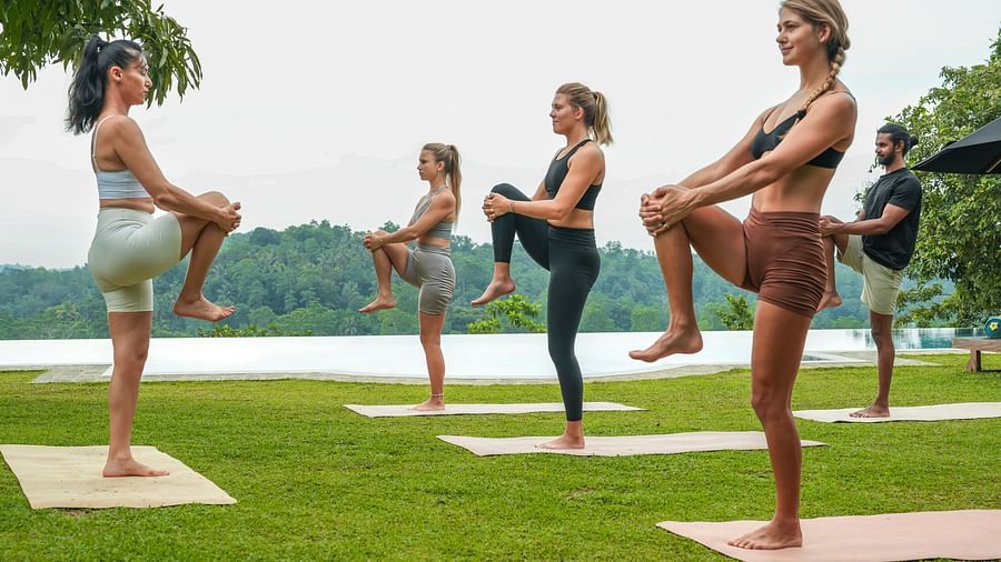 A group of women practising yoga on a green lawn overlooking a scenic lake and hills in the background - Heavensa Villas and Suites by the Clarks, Galle