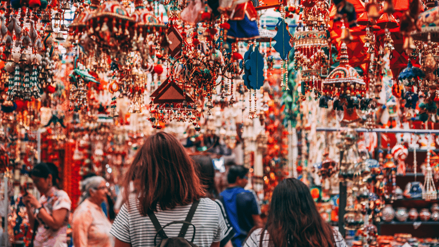 Shoppers browsing colourful handcrafted hanging decorations and artisan souvenirs at a vibrant local market.