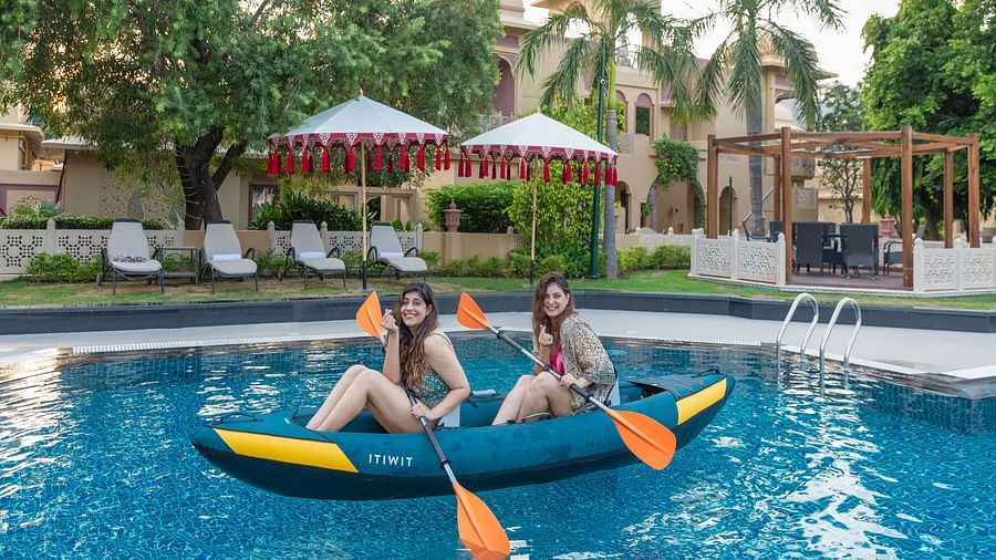 two women sitting in a kayak holding the oars that is kept in the swimming pool - Heritage Village Resorts & Spa, Manesar