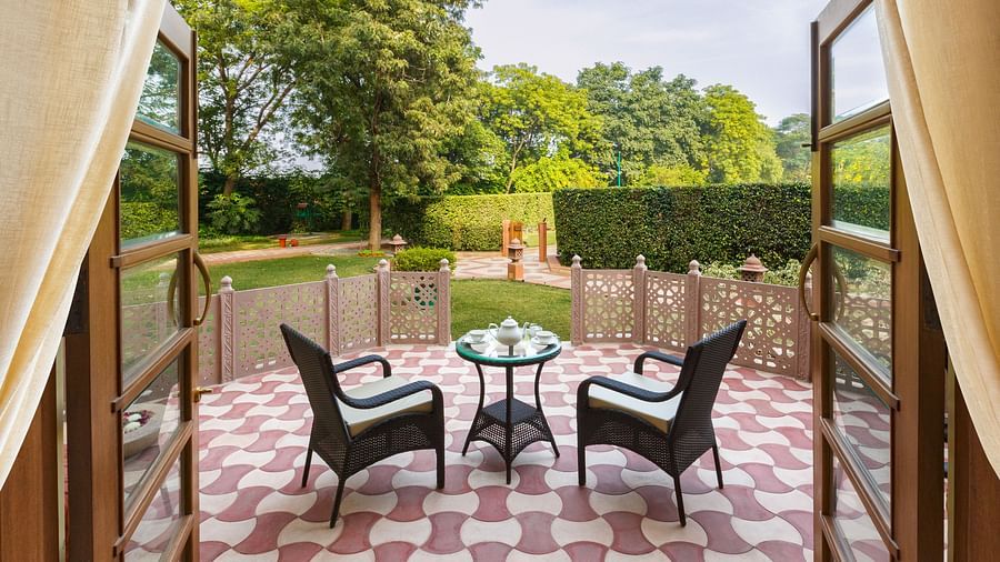 An image of a balcony with two chairs and a tea table from where a lawn could be seen - Heritage Village Resorts & Spa, Manesar
