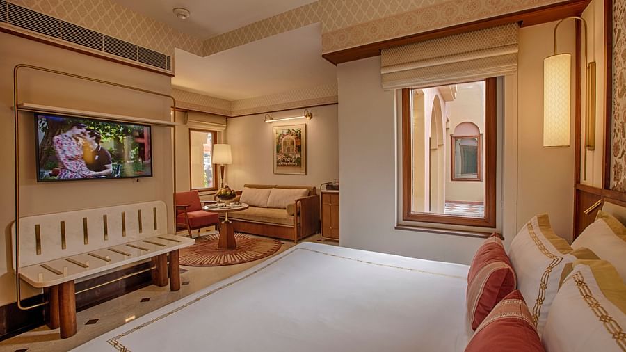 A beautifully designed bedroom with a king-sized bed adorned with soft linens, a lounge chair, a wooden centre table, and large windows with natural light