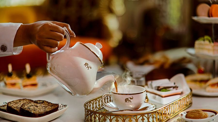 A sophisticated high tea arrangement with a white teapot pouring tea into a fine china cup, accompanied by pastries, sandwiches, and elegant tableware