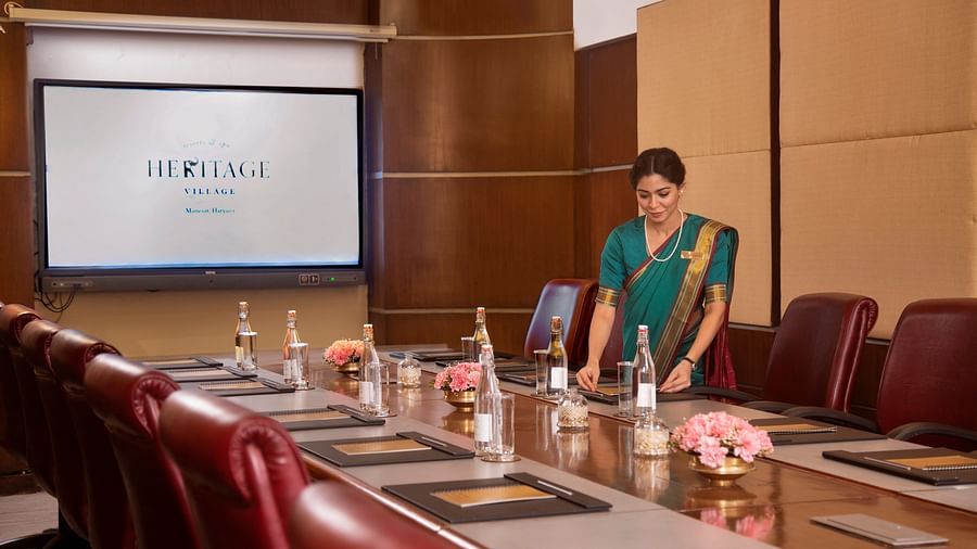 A modern boardroom setup featuring leather chairs, a wooden conference table with notepads, water bottles, floral decor, and a large presentation screen