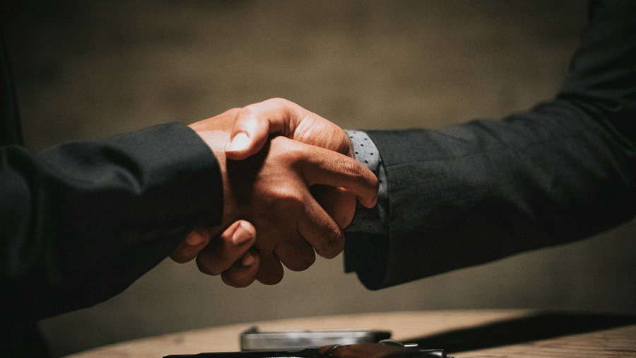 A close-up of two people in dark suits shaking hands over a table | HHI Varanasi
