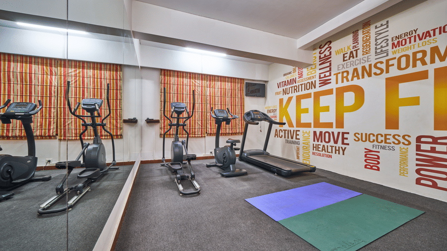 A fitness centre with elliptical machines, a treadmill, exercise mats, and a wall with typography | HHI Varanasi