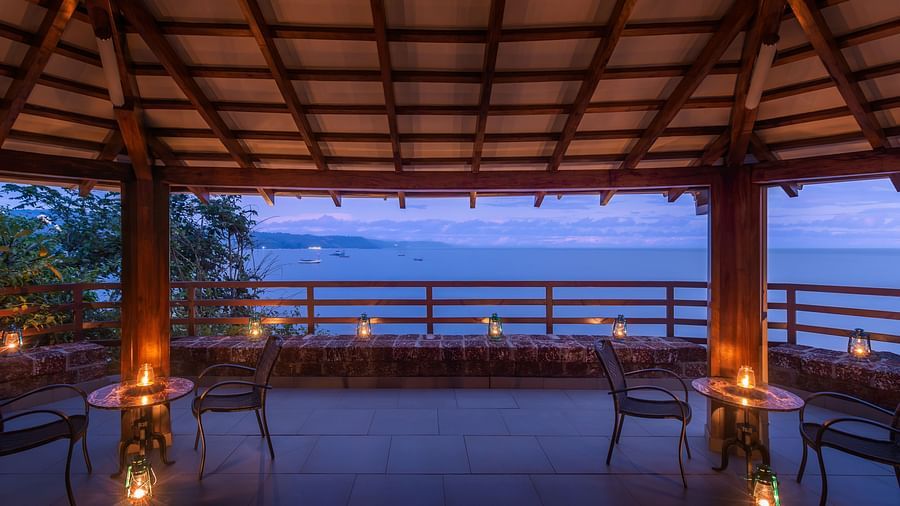 A wide-angle shot of of a gazebo overlooking the ocean seen featuring a candle light seating arrangement - Highland Sarovar Portico, Sindhudurg