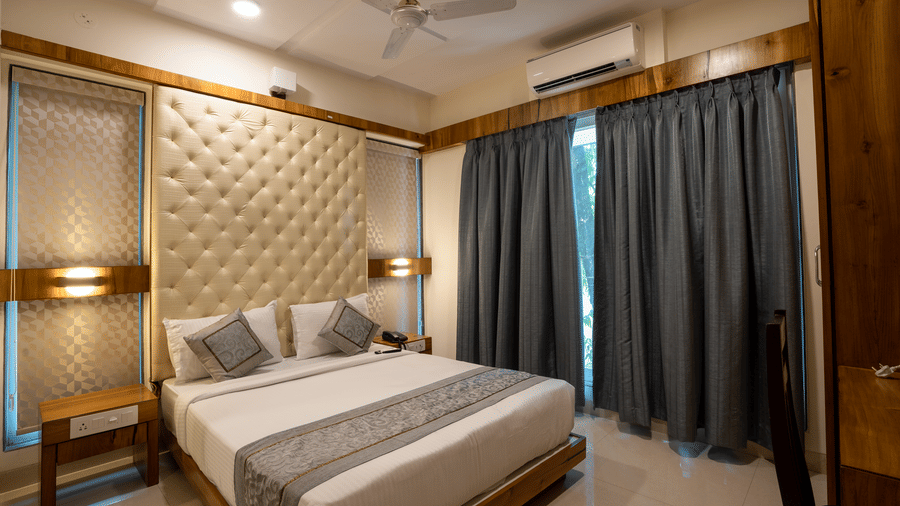 A bedroom at one of the service apartments of Home2 India featuring a plush bed next to a curtained window under warm lighting