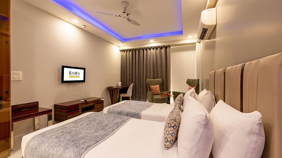 Twin beds in a room with ceiling lights and wooden furniture at Hotel Bawa, Gurgaon.