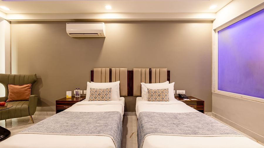 Twin beds in a room with soft lighting and a sofa chair at Hotel Bawa, Gurgaon.