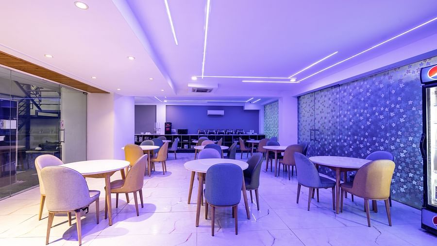 Chairs and tables placed in a dining area that has soft purple lighting at Hotel Bawa, Gurgaon.