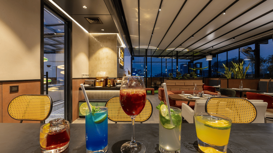 Assorted drinks placed on a counter surface at Koi Garden. The background shows the restaurant seating area with tables and chairs through the glass panels.
