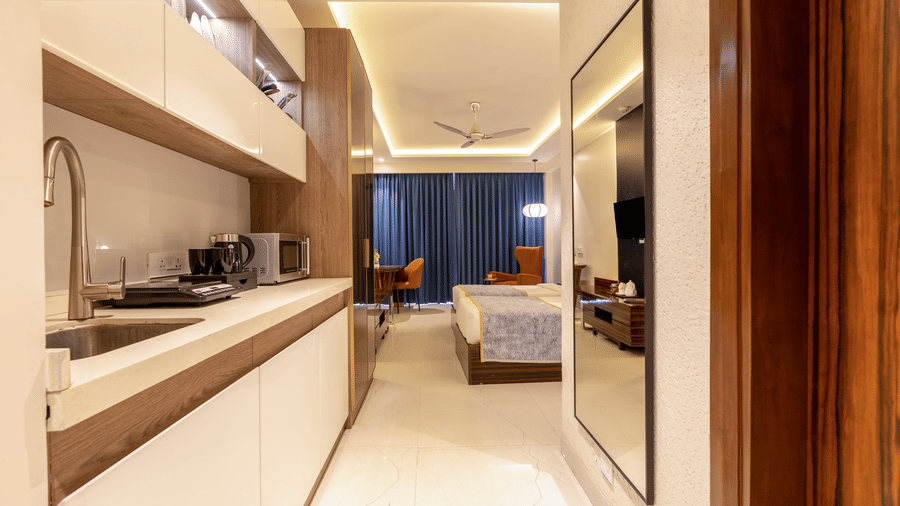 Long view of a premium kitchenette with white cabinets leading into a bright bedroom area.