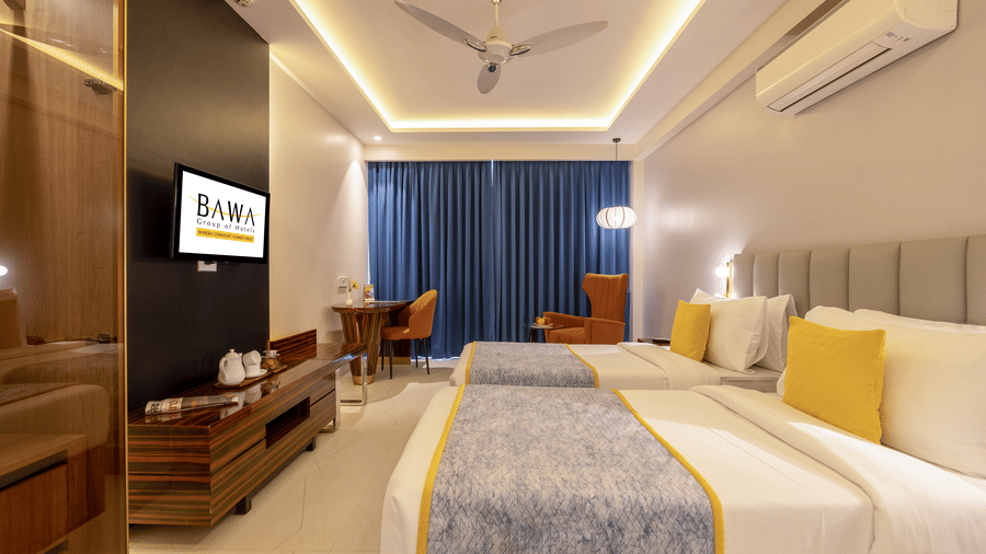 Wide shot of a hotel suite showing the television area, twin beds, and a cozy seating nook by the window.