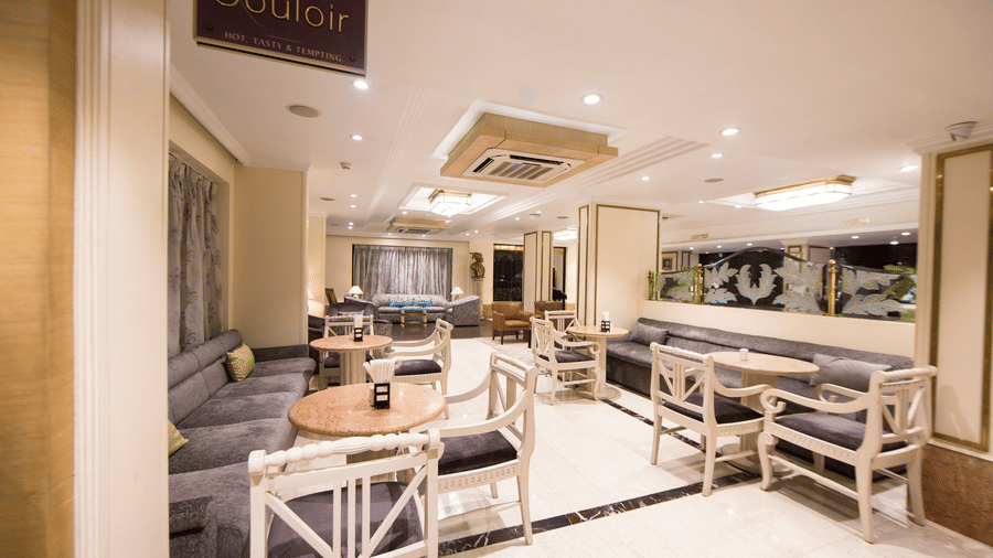 Cafe Couloir at Hotel Bawa International, Vile Parle featuring a dining area with couch and sofa chairs with tables in each setting.