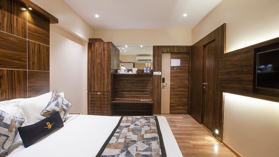 A side angle view of the Deluxe Hotel Bawa Regency, Dadar focusing on the comfy bed, wardrobe, and kettle with sugar and other amenities.
