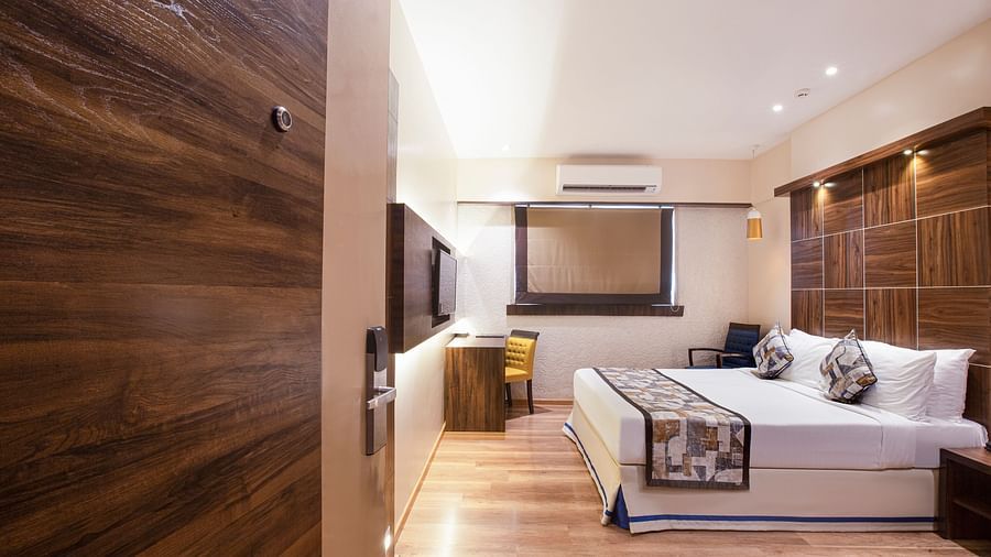 A side angle view of the Deluxe room at Hotel Bawa Regency, Dadar, featuring a comfy bed, a work desk, and a window.