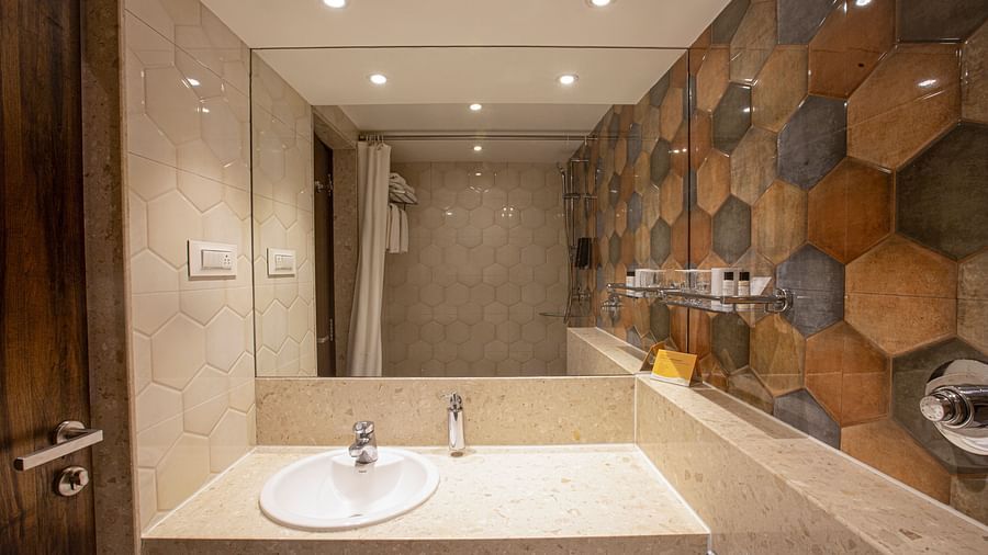 A wide-angle view of the Deluxe bathroom at Hotel Bawa Regency, Dadar, focusing on the handwash area with a large mirror.
