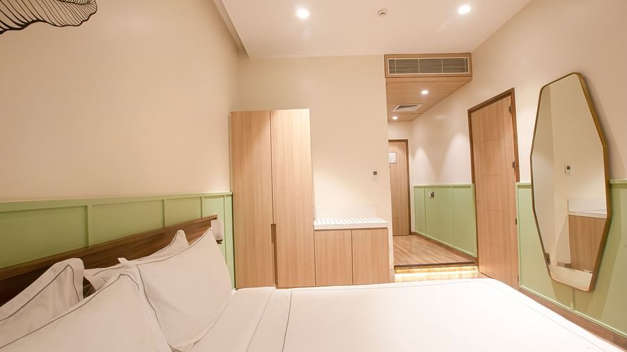 A side wide-angle view of the Superior Deluxe room at Hotel Bawa Regency, Dadar, featuring a cupboard, a passage leading to the door, and a mirror.