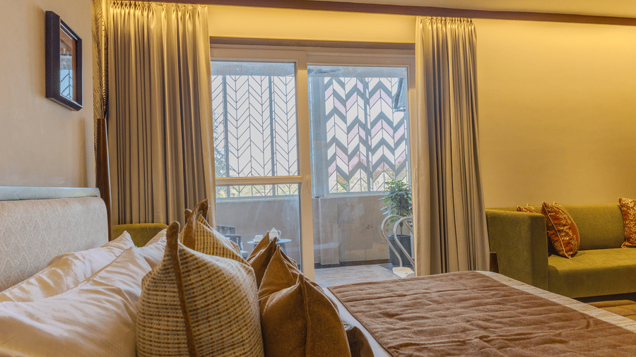 A lit bedroom with a king size bed, sheer curtains and direct access to a private balcony at Hotel Bawa, Udaipur