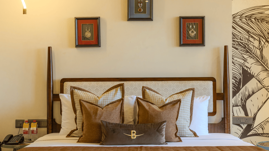 King size bed with layered decorative cushions, ambient bedside lighting and framed wall art at Hotel Bawa, Udaipur.