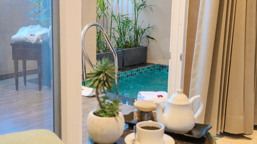 Private plunge pool surrounded by lush green plants with a tea set placed beside it in the Royal Suite at Hotel Bawa, Udaipur.