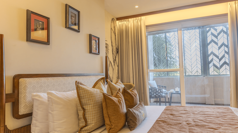 Bright bedroom with a king size bed, mustard bench, potted indoor plants and access to a private balcony at Hotel Bawa, Udaipur.