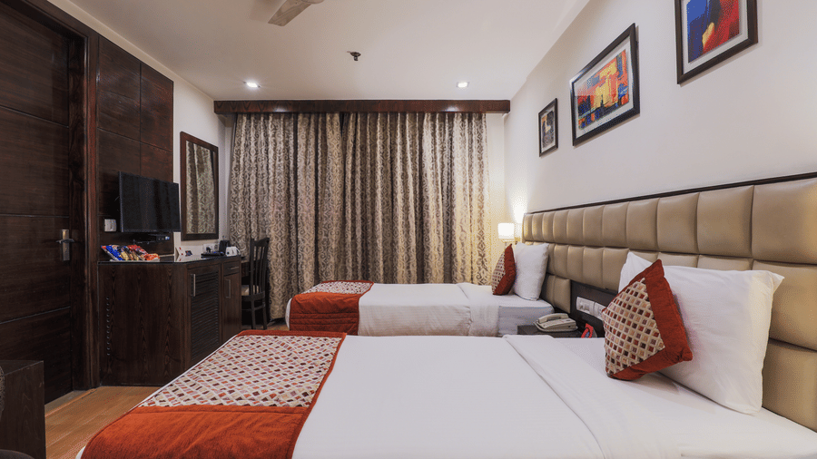 A cosy hotel bedroom features 2 large, neatly made beds with colourful pillows and a patterned red runner - Hotel Bluestone Prime (Nehru Place), New Delhi