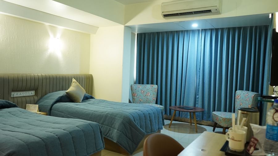 An image of a bedroom with twin beds, AC, table and chair, and two single sized sofa