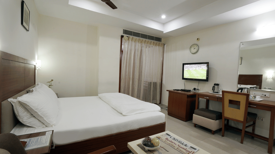 Deluxe room with a comfortable bed, wooden furnishings, television and work desk at Hotel Geetha Regency, Guntur.