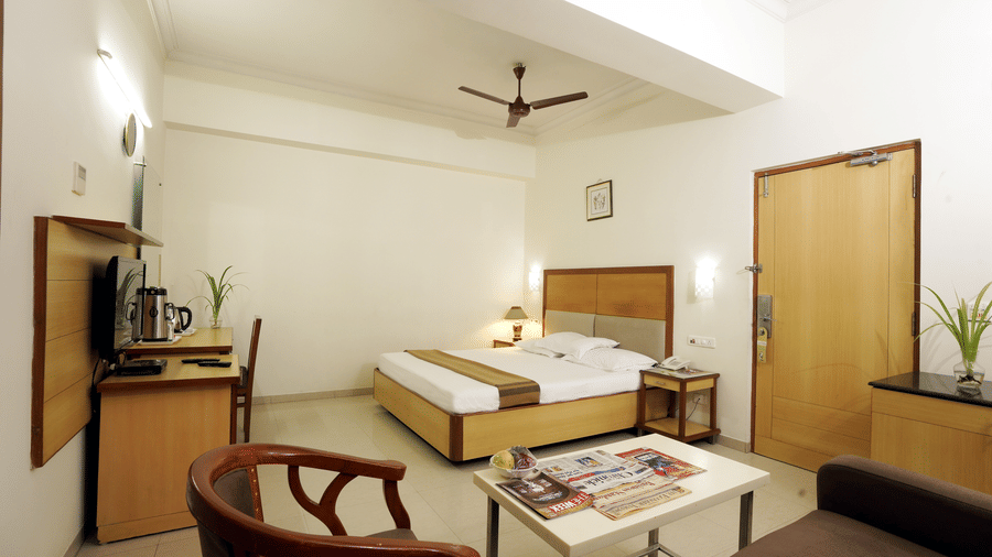 Suite room with a comfortable bed, seating area, table and wooden furnishings at Hotel Geetha Regency, Guntur.