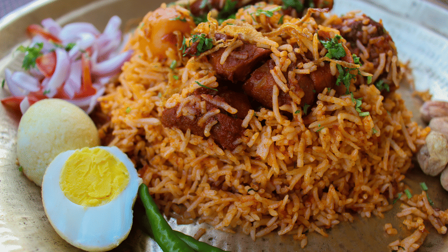 A serving of Arcot Mutton Biryani at Hotel Ivory Tower, Bangalore, featuring rice cooked with mutton, boiled egg and a light salad on the side.