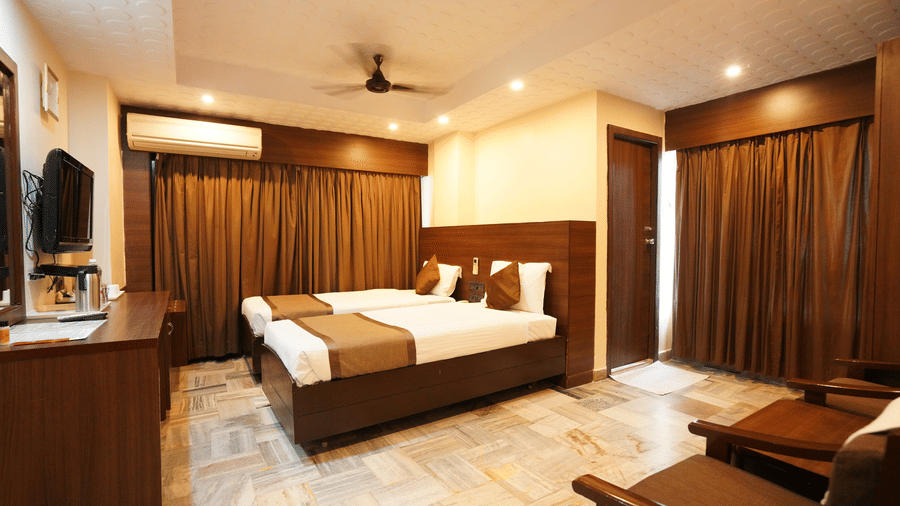 Deluxe room interior with a comfortable bed, wooden furnishings and warm lighting at Hotel Jaya Residency, Kakinada.