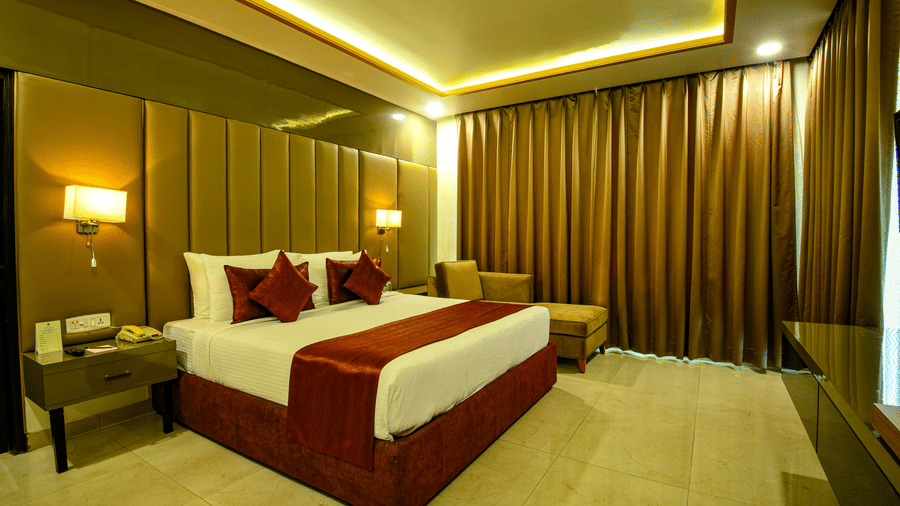 Hotel room at Hotel Kanha Shyam, Prayagraj, with a king-sized bed, warm lighting and a mirrored feature wall.