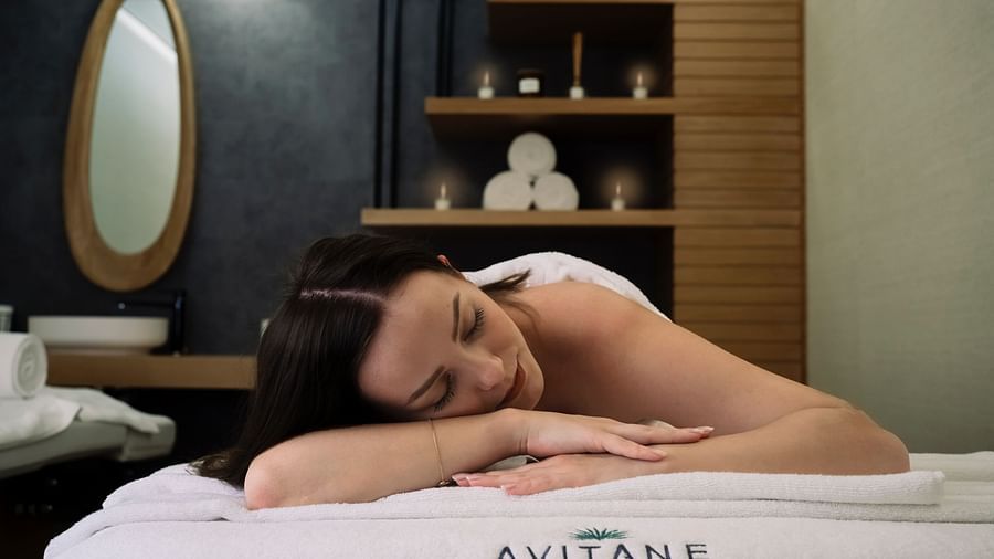 a woman laying on her stomach on a spa bed with the backdrop of towels and essential oils kept in a shelf
