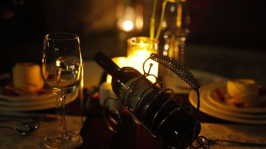 a wine bottle kept in a wine stand amidst a candle light dinner setting with candles, wine glasse and fine cutlery.