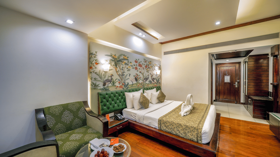 A spacious bedroom at Hotel Saffron Leaf, Dehradun, featuring a plush bed with a headboard, an accent wall with painted birds, elegant furnishings and a wooden floor. 
