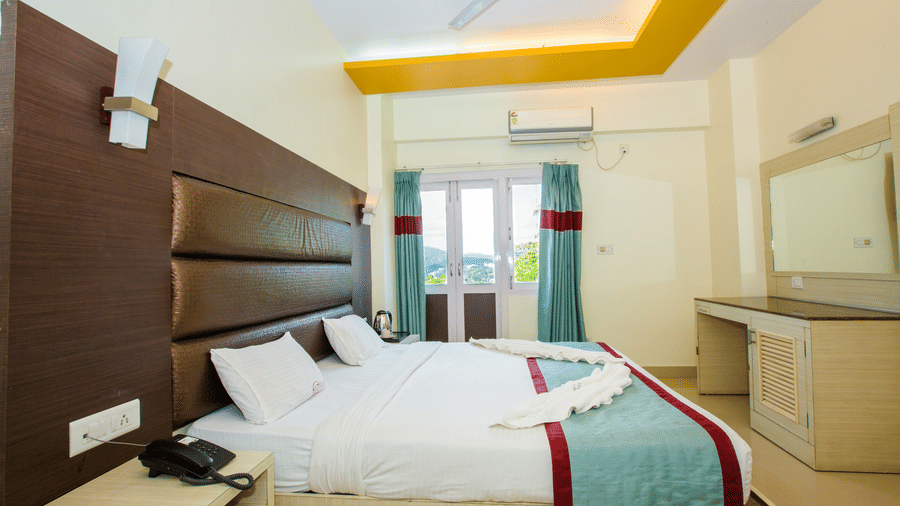 Interiors of Sea View Room, one of finest Port Blair Stay at Hotel Shompen, featuring a large bed, upholstered headboard, dressing table, and a large window offering outdoor views.