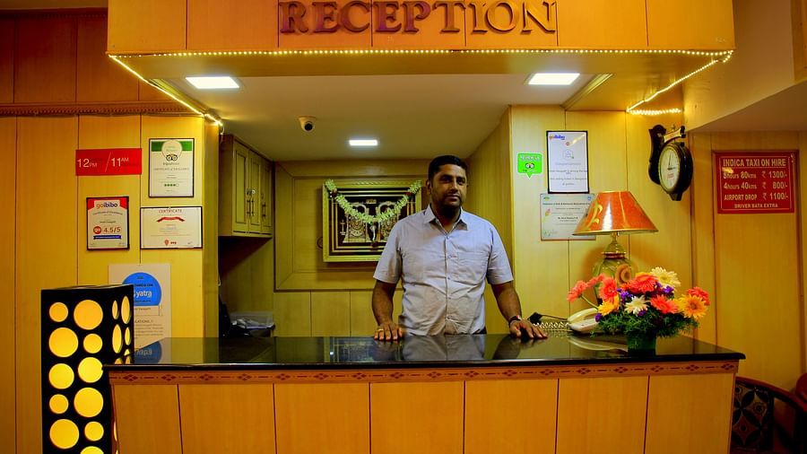 a man standing by the reception counter making a call at Hotel Swagath, Bangalore