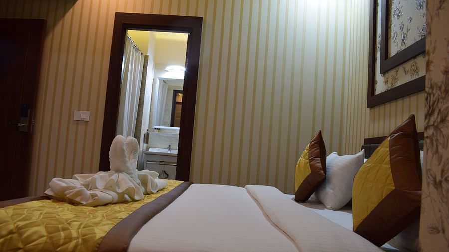 A side view of a spacious bed with a door in the background leading to the washroom at Hotel Uday Palace.